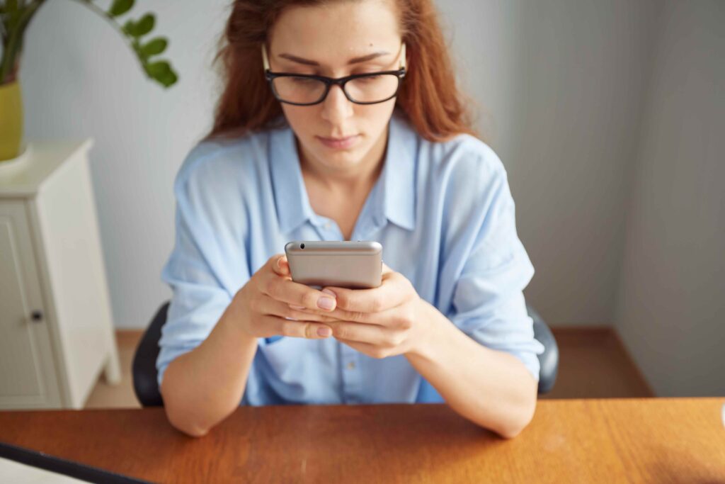 cropped-view-portrait-cute-redhead-girl-texting-cell-phone-wooden-desk_11zon
